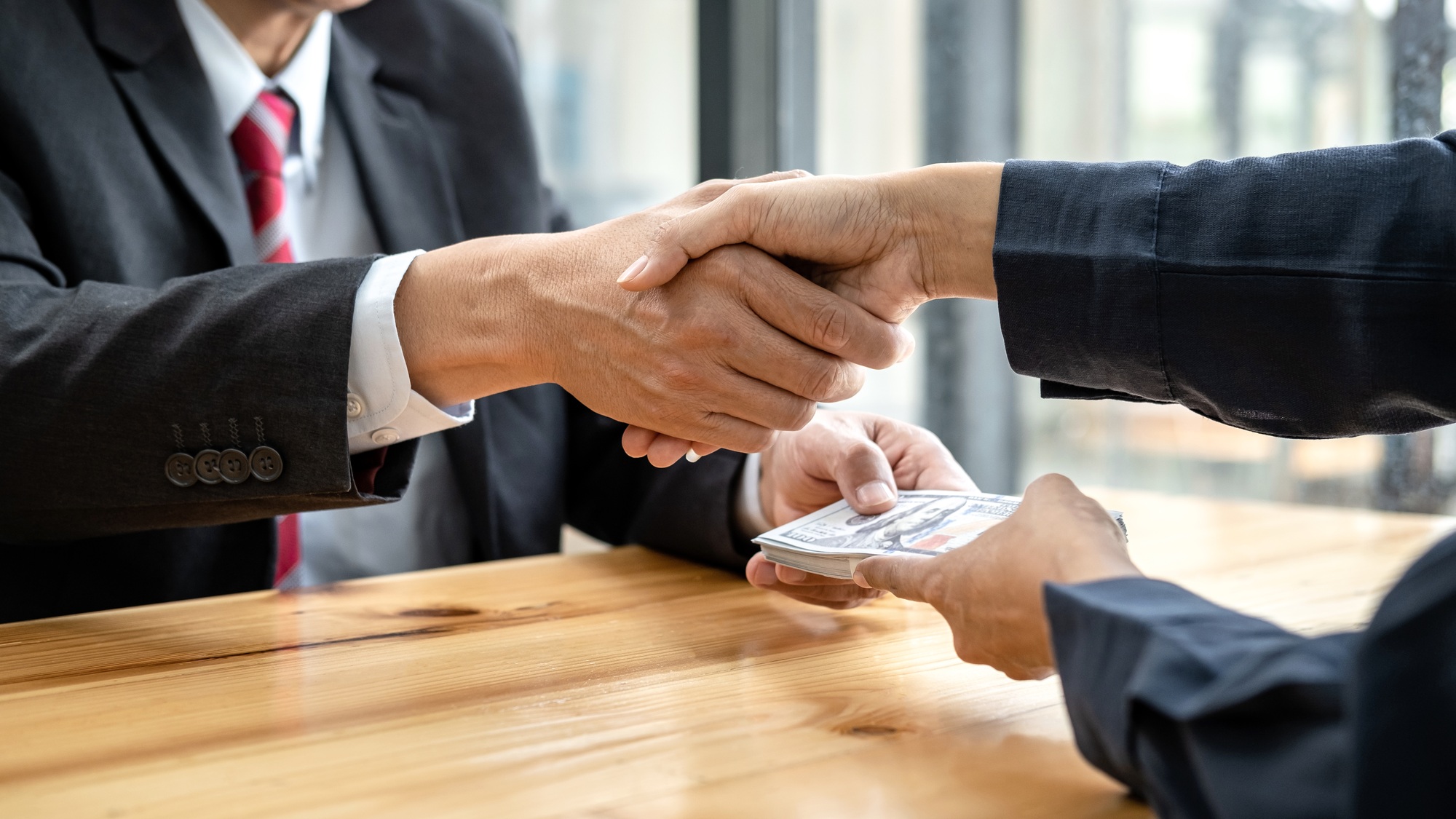 Businesspeople shaking hands to receive banknote money and terms of contract from bribe employer