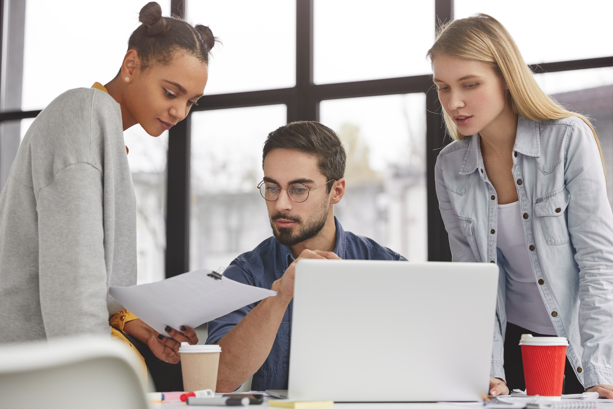 Group of friendly talented coworkers discuss together work questions, sit against modern office spac